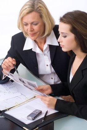 two women in business attire looking at paperwork