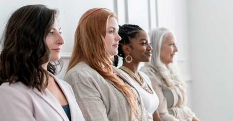 Four women of different ages and ethnicities sit in a row, facing to the right against a white background, each embodying the importance of being present in the moment.