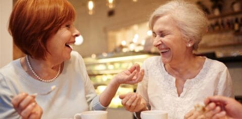 Two senior women laughing together at a cafe table.